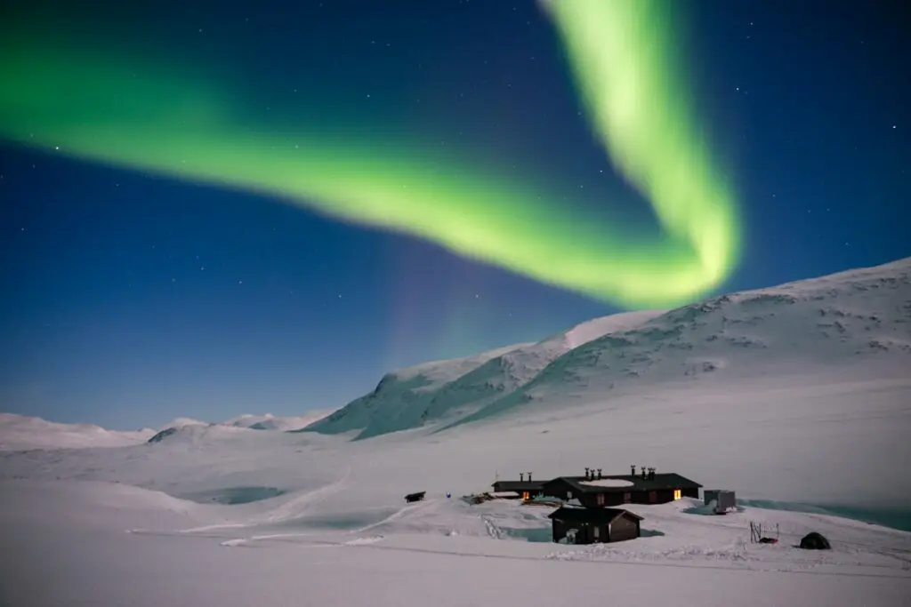 northern lights over snow-covered mountains and cabins in Swedish Lapland