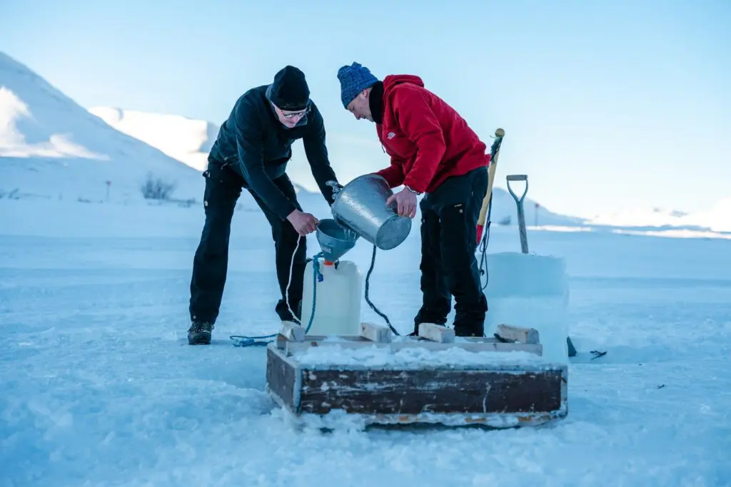 two men collecting water from ice in snowy landscape