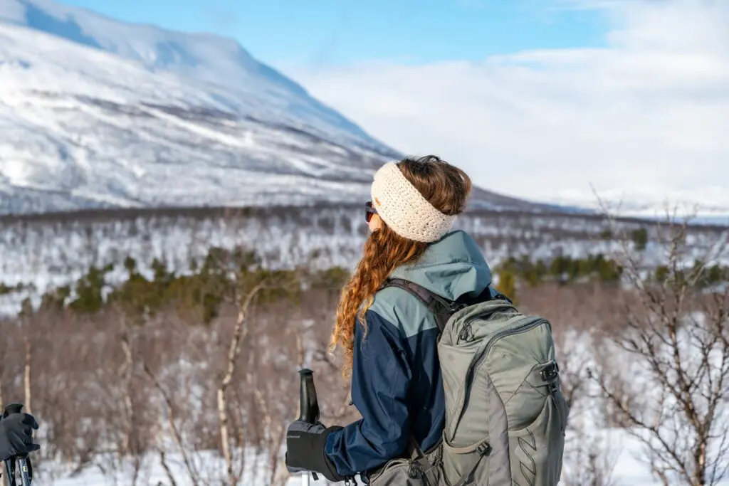 woman with backpack and trekking poles looking at snowy mountains