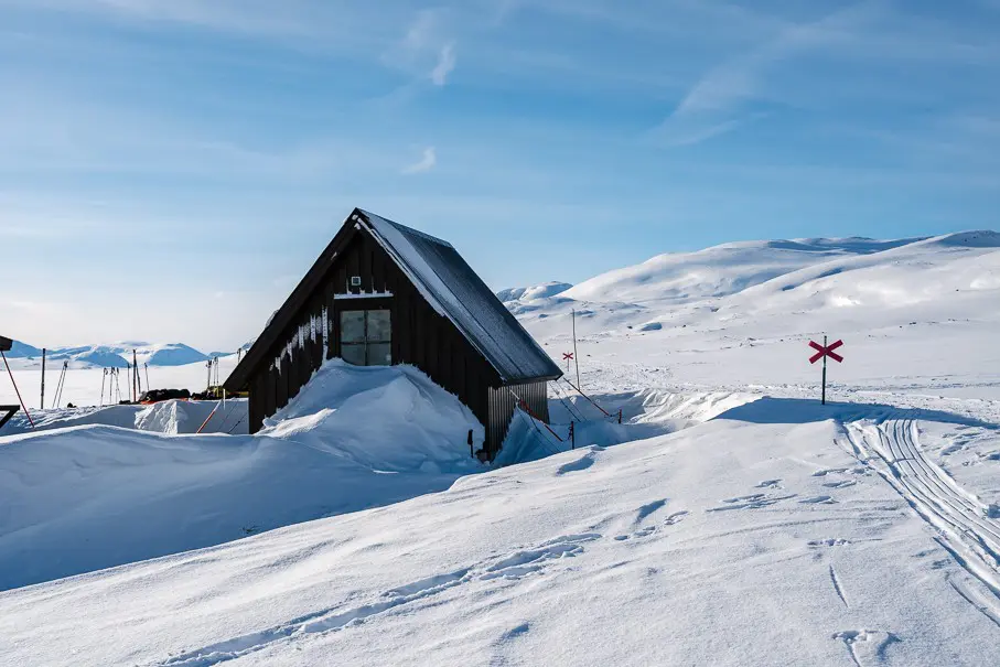 wooden cabin in snowy Swedish Lapland mountains with ski tracks